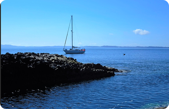 Sailboat anchored near a rocky shoreline on a bright, sunny day.